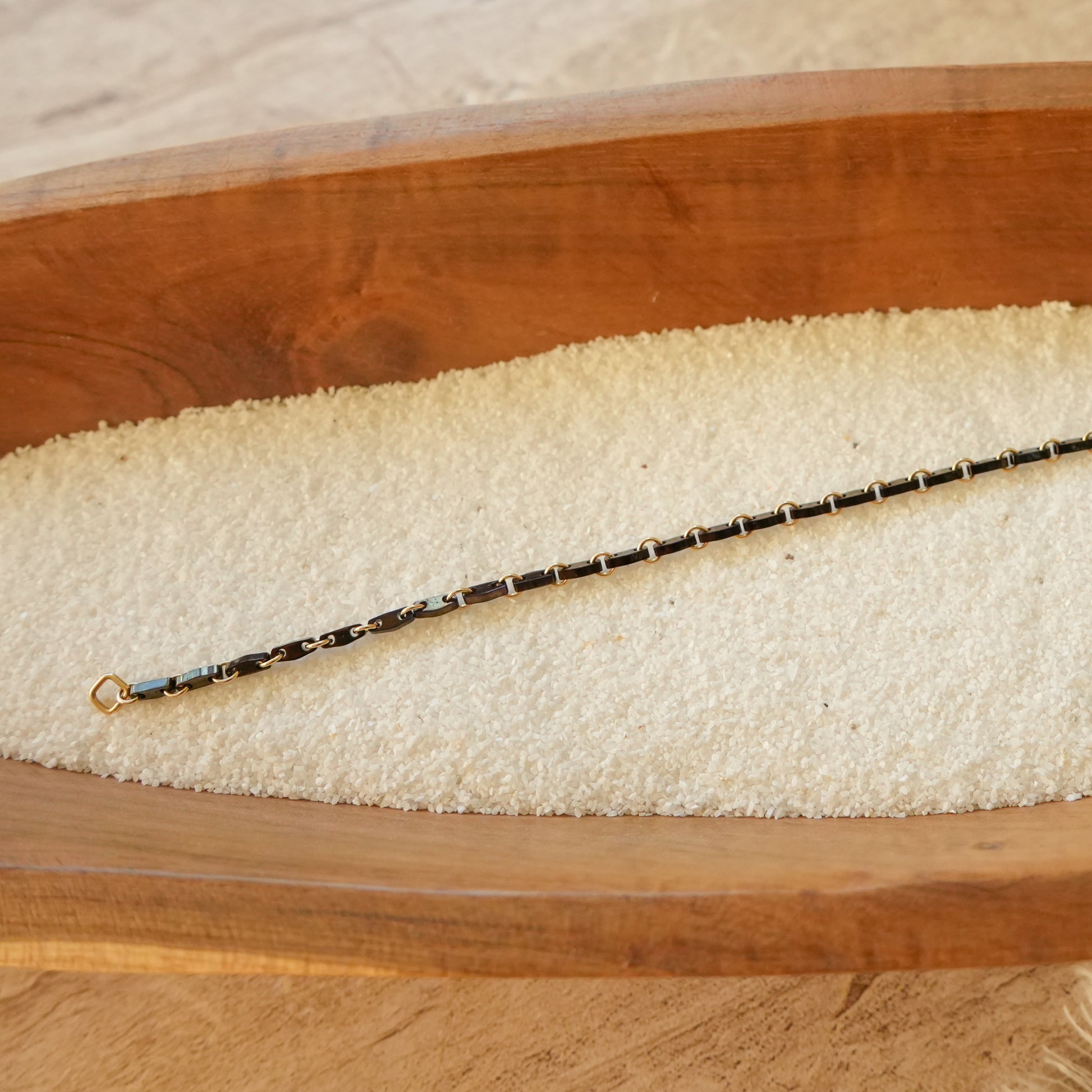 black bracelet with Japanese glass beads and circle chain links on white sand in a wooden tray