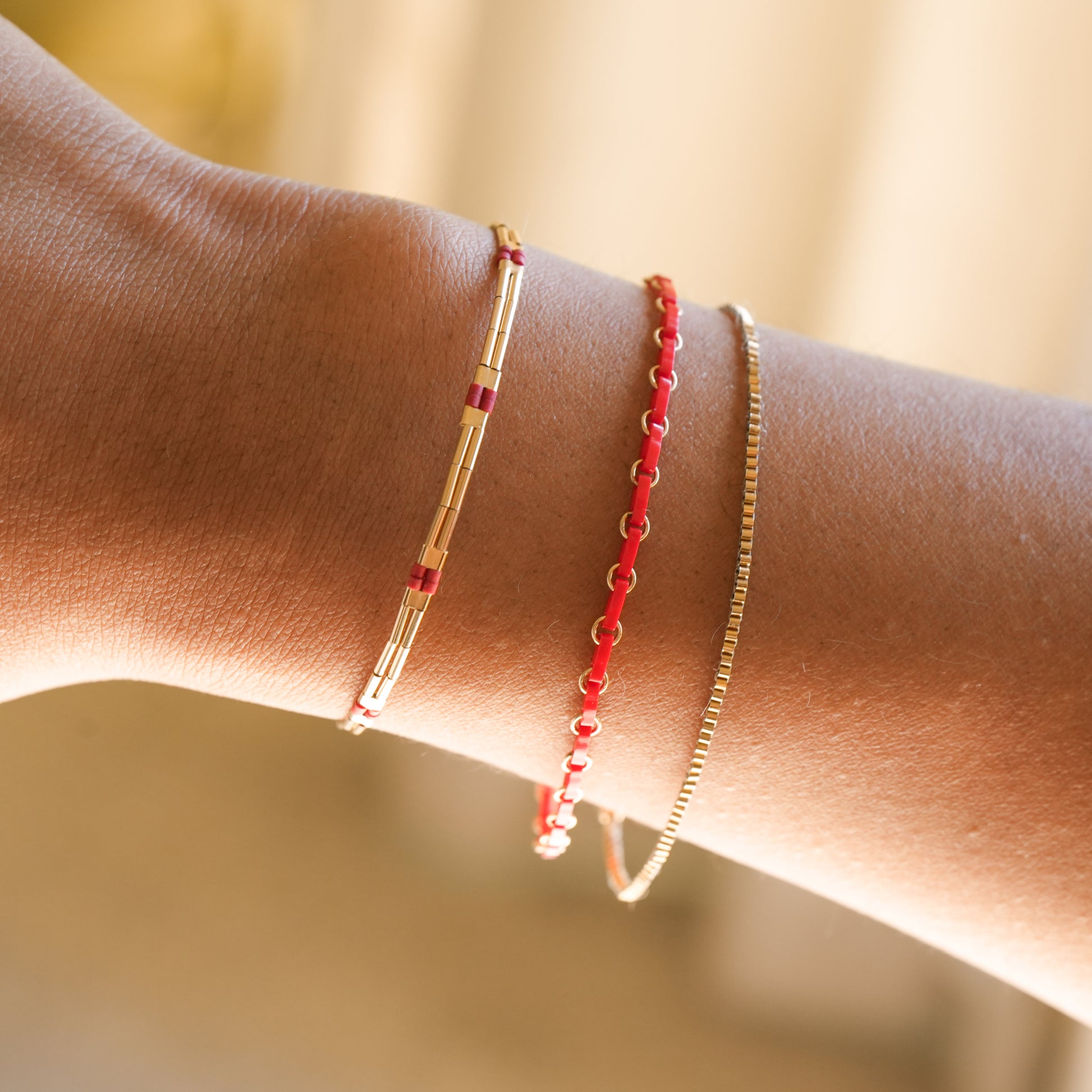 woman's wrist with 3 bracelets with red and gold beads