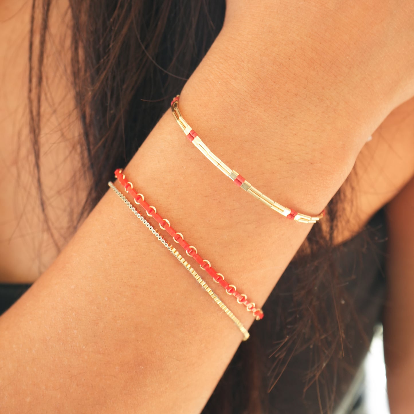 woman's wrist with red and gold-filled beaded bracelets