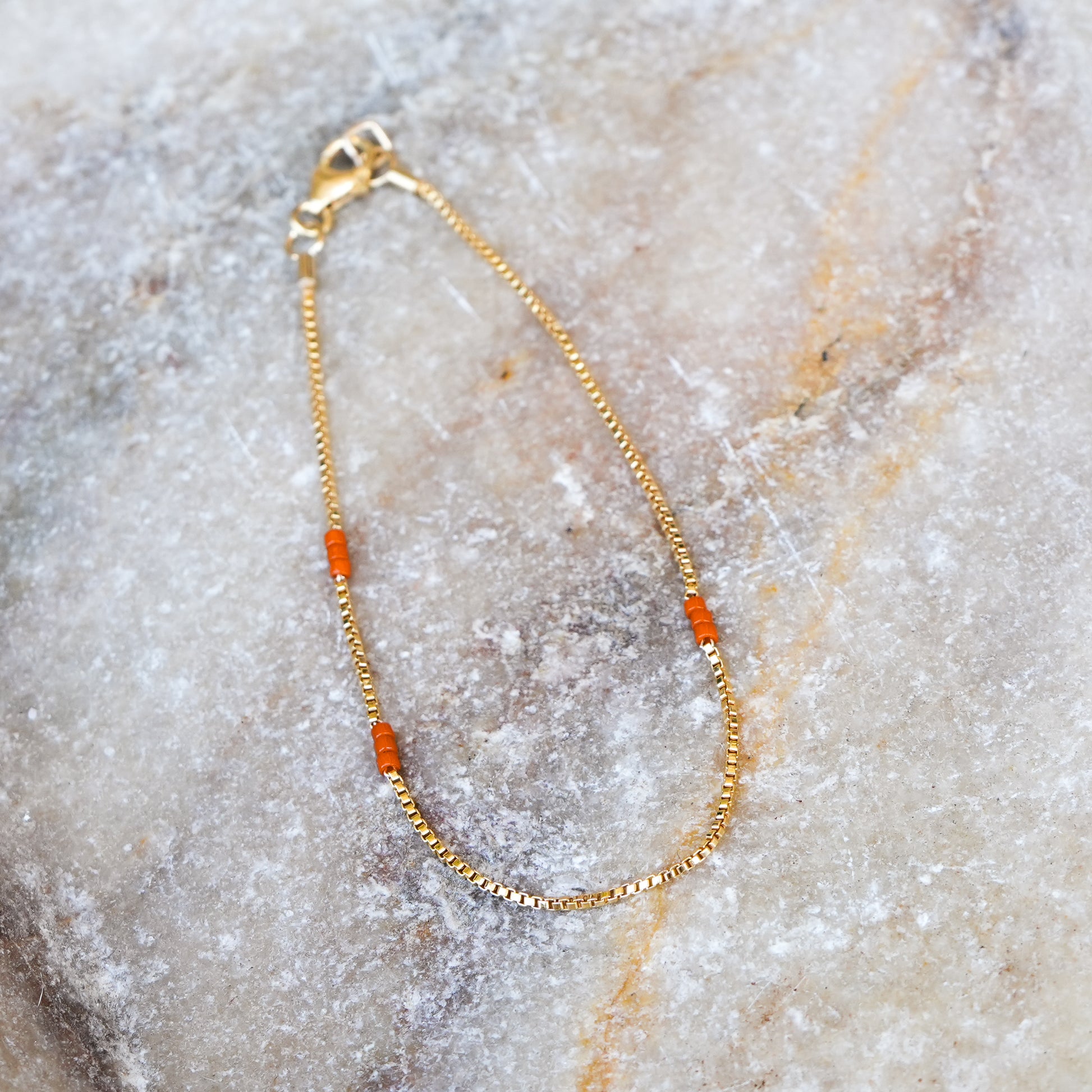bracelet with gold-fill chain and 3 sets of 3 Japanese seed beads on a stone surface