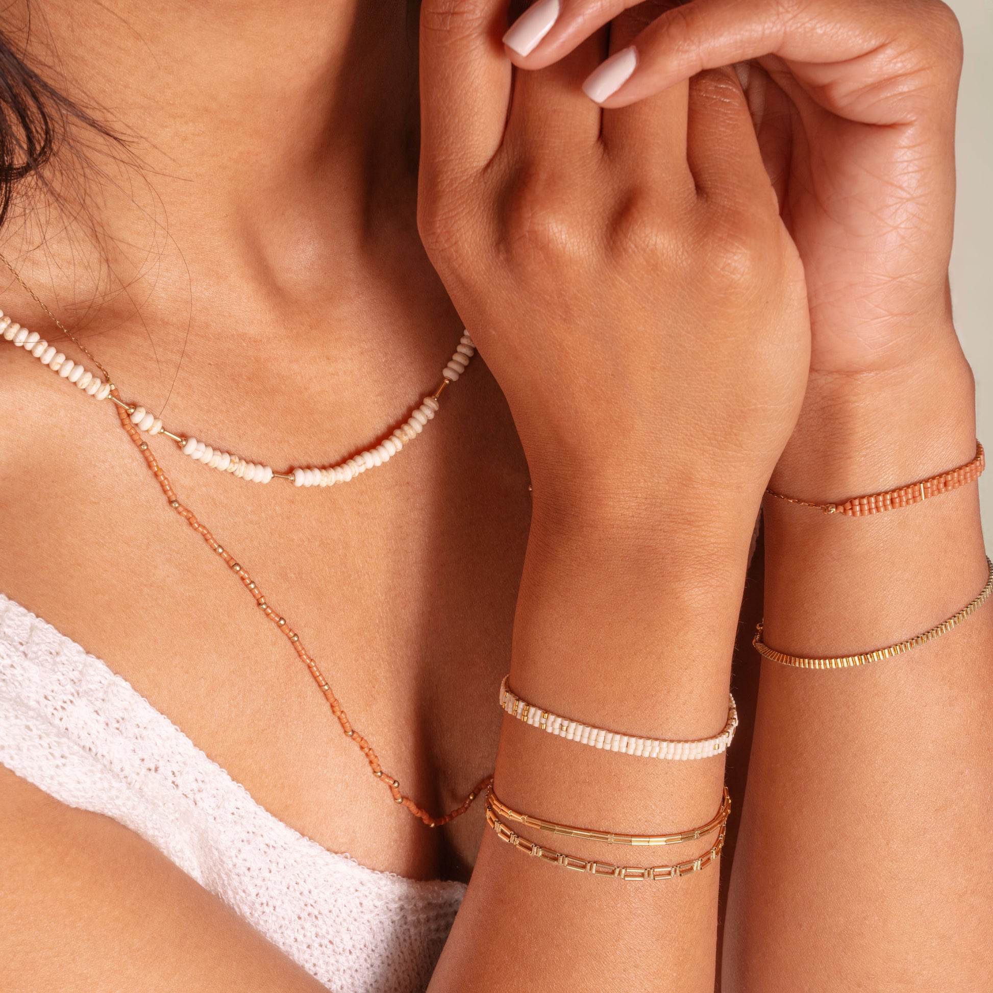woman with both arms up showcasing multiple bracelets and necklaces with coral and white colored beads