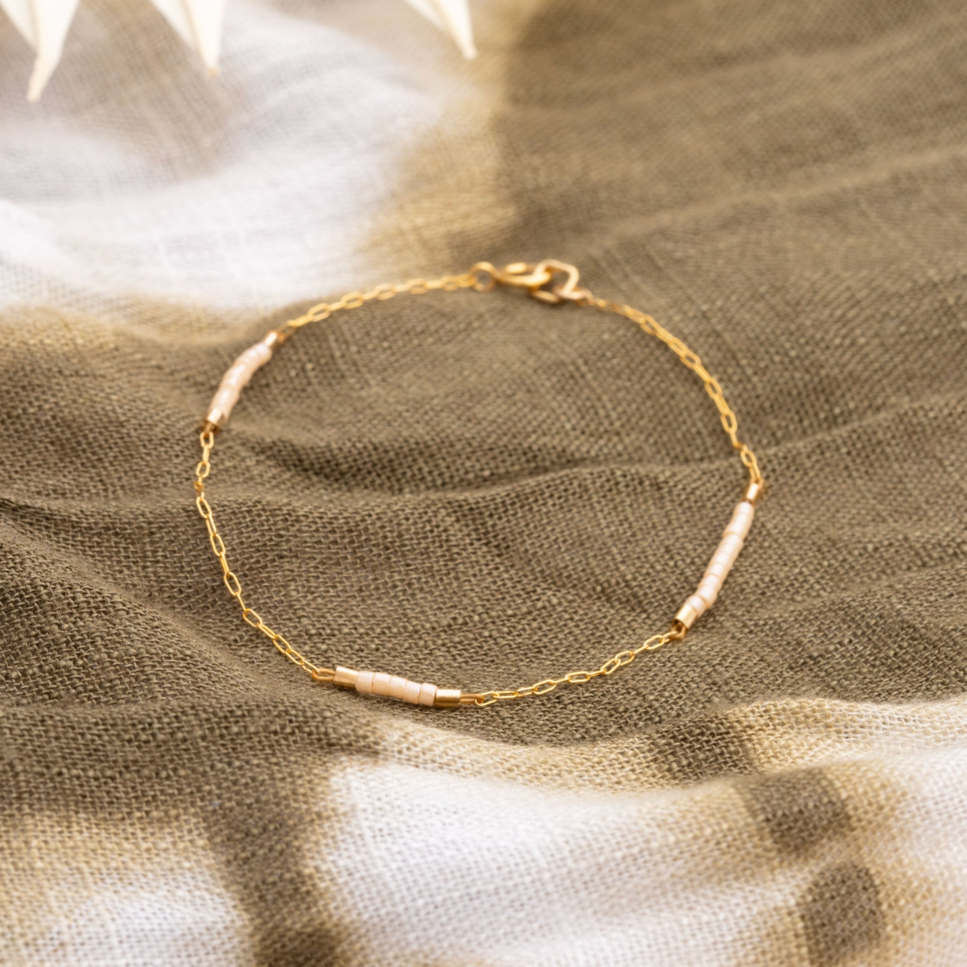 close up view of a bracelet with a gold-fill chain with Miyuki glass beads resting on a brown and cream dyed cloth