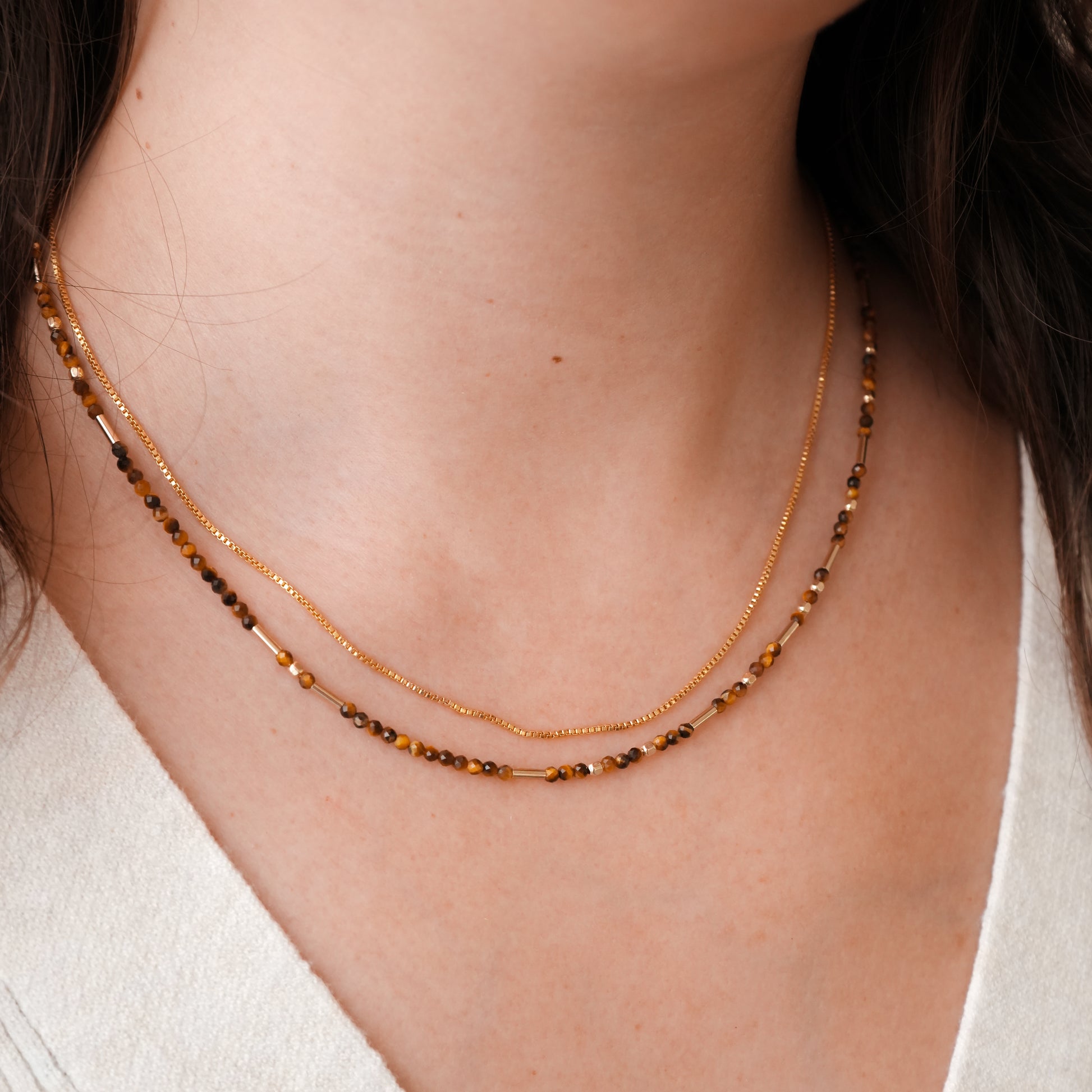 woman wearing a tiger's eye beaded necklace and a gold chain necklace