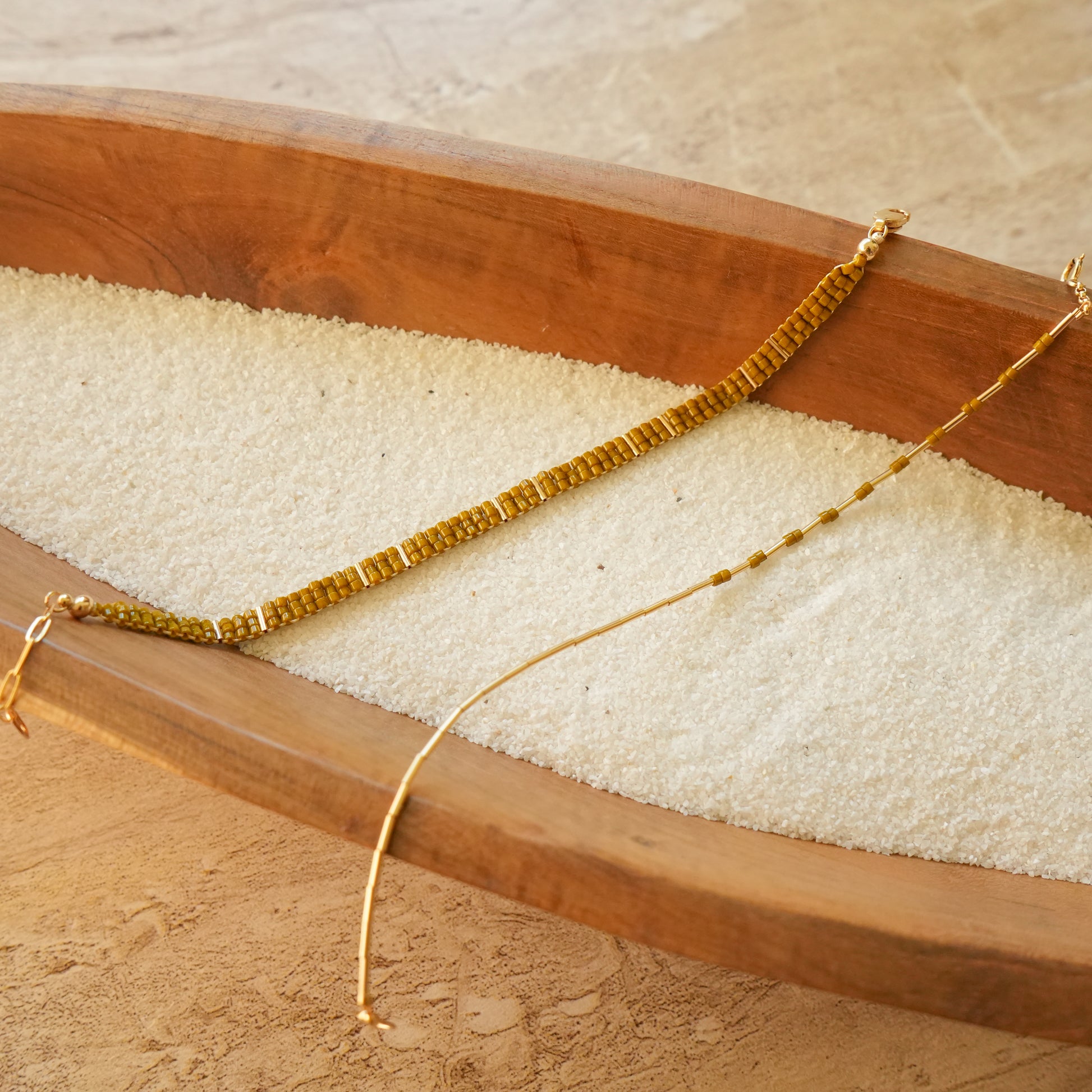 unclasped chartreuse beaded bracelets on a wooden tray with white sand