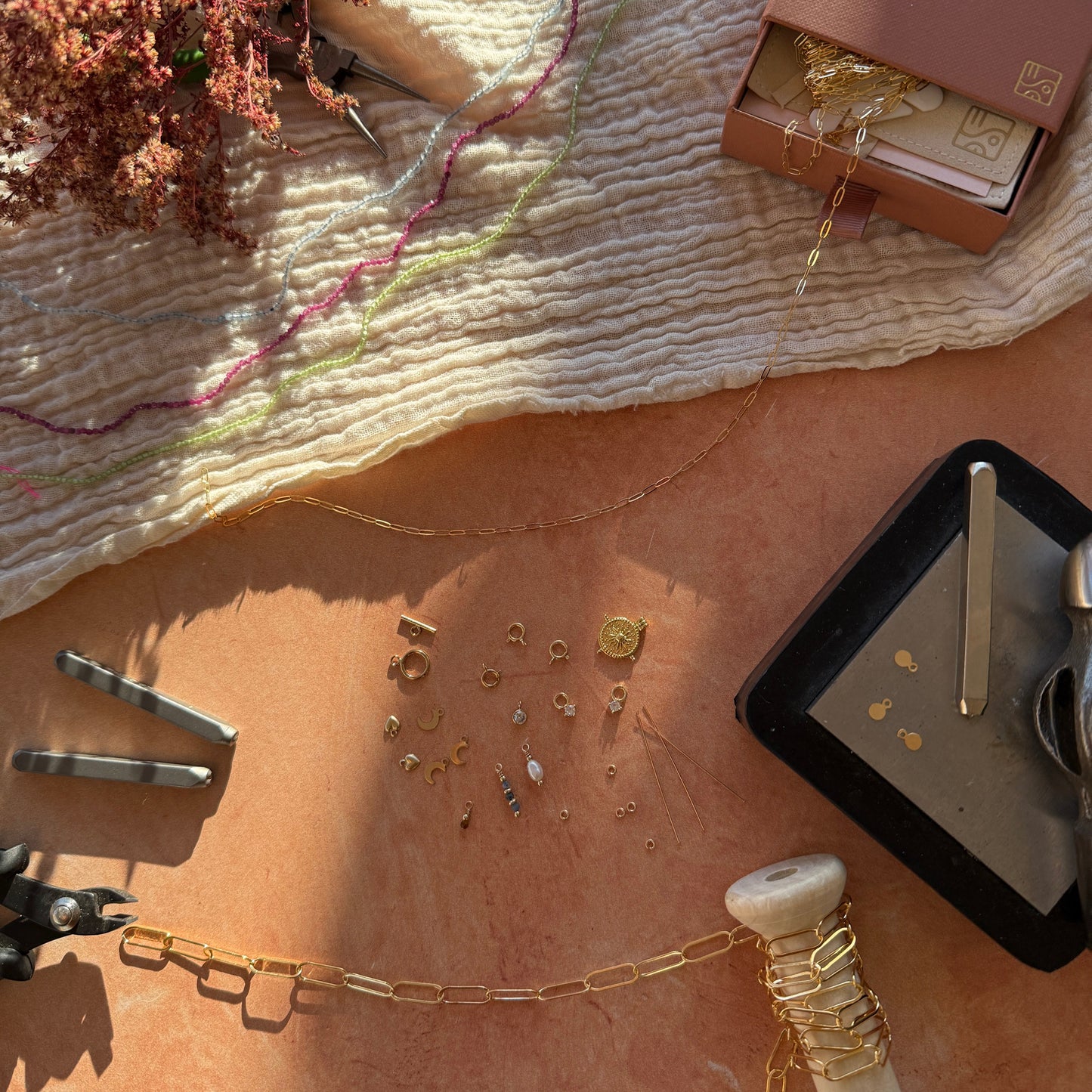 flat lay of workshop tools showing mixed gold chains, beads, packaging, stamping block