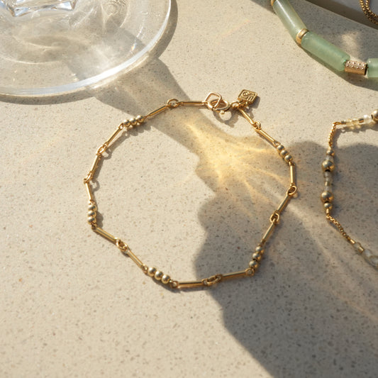 gold-fill beaded bracelet with logo charm next to a wine glass